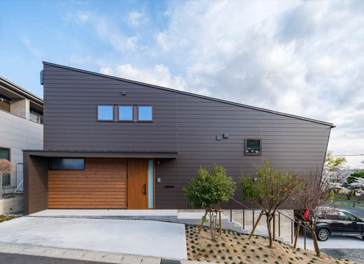 坂の斜面と平行な片流れ屋根とダークブラウンの外壁の住宅